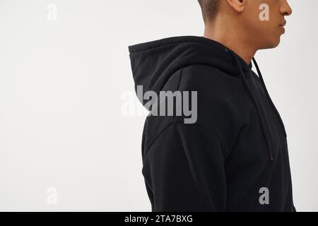 Zugeschnittene Ansicht eines afroamerikanischen Mannes in schwarzem Hoodie im Profil vor weißem Hintergrund, Modekonzept Stockfoto