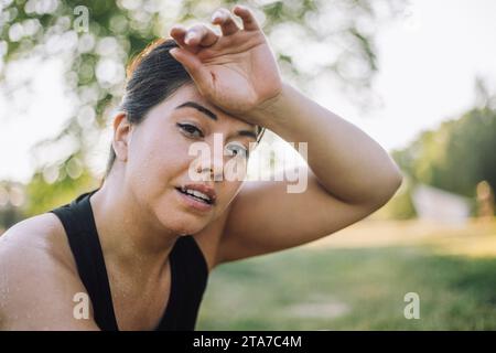 Porträt einer schwitzenden Frau mit Kopf in Hand im Park Stockfoto