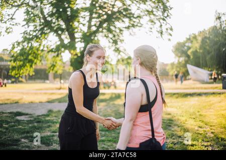 Lächelnde Frau beim Handschlag mit einer Freundin im Park Stockfoto