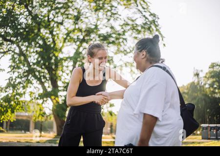 Glückliche junge Frau beim Handshake mit übergroßer Frau im Park Stockfoto