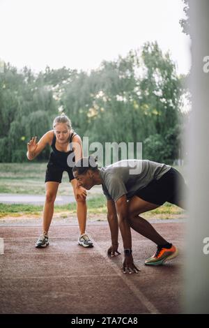 Weibliche Trainerin, die dem Mann bei der Vorbereitung auf den Sprint auf der Laufbahn hilft Stockfoto