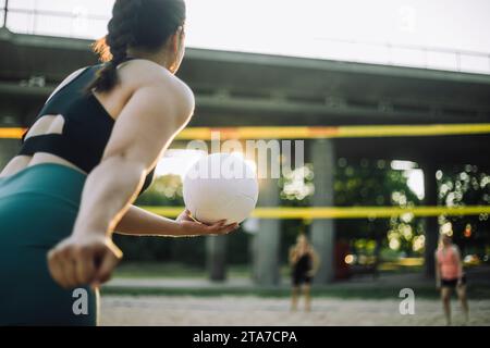 Frau, die sich auf das Servieren vorbereitet, während sie mit Freunden Volleyball spielt Stockfoto