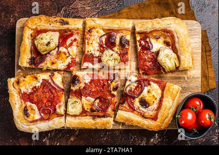 Vegetarische Blätterteigpizza mit Artischocke, Mozzarella, Tomaten und Käse auf einem Holzbrett. Dunkler Hintergrund. Draufsicht. Stockfoto