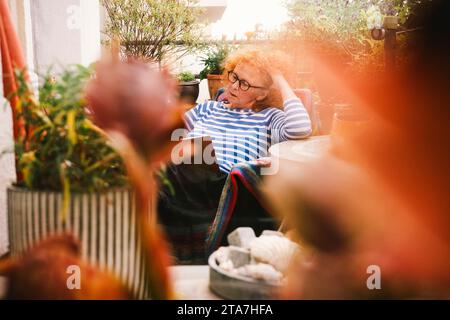 Eine ältere Frau liest ein Buch, während sie auf dem Balkon sitzt Stockfoto