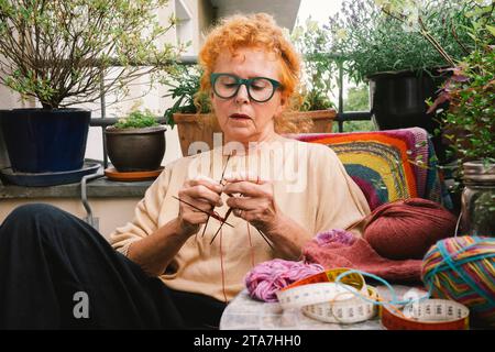 Ältere Frau strickt Pullover, während sie auf dem Balkon sitzt Stockfoto