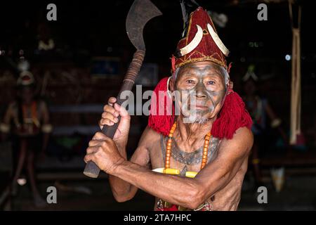 Älterer Krieger aus dem Stamm der Konyak in traditioneller Kleidung mit tätowiertem Gesicht und traditioneller alter Axt in den Händen, Nagaland, Indien Stockfoto