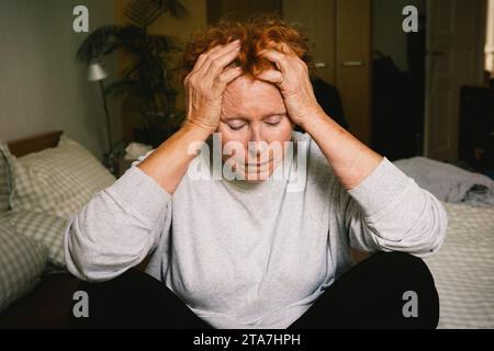 Depressive Seniorin, die mit dem Kopf in den Händen im Schlafzimmer sitzt Stockfoto