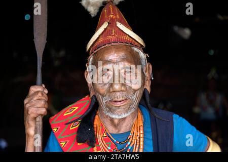 Dorfchef des Konyak-Stammes in traditioneller Kleidung mit Tätowierungen im Gesicht in einem Holzhaus aus Bambus, Nagaland, Indien Stockfoto