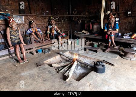 Älteste, Männer, Krieger aus einem Konyak-Stamm mit Stammestattoos auf Gesichtern und traditionellen Hüten, Halsketten, Ohrringen, im Haus sitzend, Nagaland, Indien Stockfoto