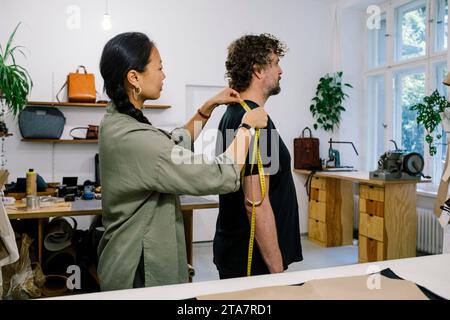 Seitenansicht einer Modedesignerin, die den Kundenstand in der Werkstatt misst Stockfoto