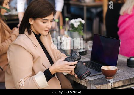 Porträt des Inhalts-Erstellers mit Kamera. Eine junge Frau hält eine spiegellose Kamera und überprüft Fotos und Videos. Stylischer Freelancer Stockfoto