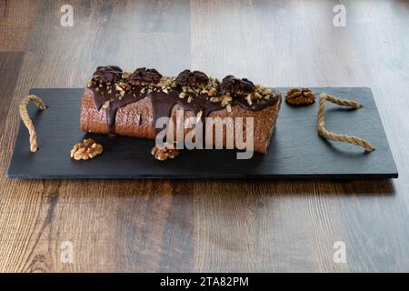 Auf einem Holzbrett, ein Schweizer Brötchen mit Haselnüssen, Buttercremefüllung und Zartbitterschokolade. Dies ist perfekt für jeden Tag oder Silvester-Leckereien. Stockfoto