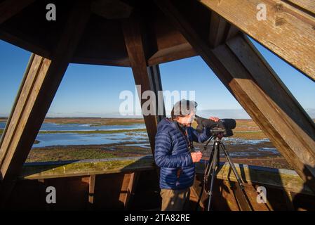 Vogelbeobachter mit Blick durch das Teleskop über die Salzwiesen der westlichen Schelde-Mündung im Naturschutzgebiet Verdronken Land van Saeftinghe, Niederlande Stockfoto