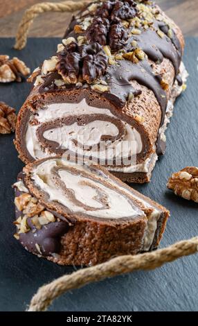 Ein Schweizer Brötchen in Scheiben geschnitten und garniert mit dunkler Schokolade, Haselnüssen und Buttercremefüllung auf Holzschiefer. Perfekt für jeden Tag oder Neujahr. Stockfoto