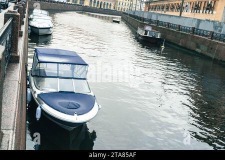 Boote und Schnellboote zahlreiche Boote und Schnellboote liegen in einem ruhigen Fluss Stadtkanal, umgeben von einer lebhaften Stadtlandschaft im Hintergrund. Th Stockfoto