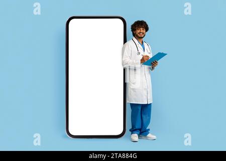 Junger indischer Doktor, der neben einem riesigen Telefon steht Stockfoto