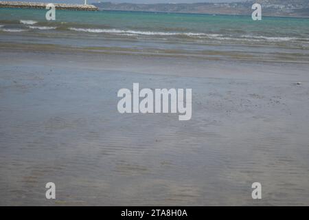 Nicht bearbeitetes Foto von friedlichem Wasserhorizont und Sandzusammensetzung. Nützlicher Sommerhintergrund mit Sandstrand mit Wasserrand Stockfoto