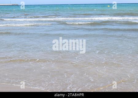 Nicht bearbeitetes Foto von friedlichem Wasserhorizont und Sandzusammensetzung. Nützlicher Sommerhintergrund mit Sandstrand mit Wasserrand Stockfoto