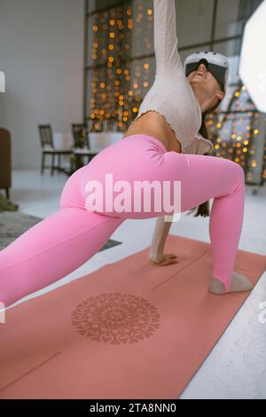 Trainieren Sie in einem pinkfarbenen Sportoutfit mit einem Virtual-Reality-Headset vor der Kulisse eines Weihnachtsbaums. Stockfoto