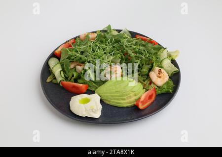 Garnelensalat, Avocado, Salat und Kirschtomaten. Leckeres Gemüse gemischte Blätter mit gegrillten Garnelen in schwarzer Platte auf weißem Hintergrund. Stockfoto