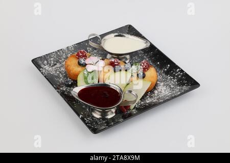 Syrnyky von Hüttenkäse mit Beerenmarmelade, Sauerrahm und Beere auf dunklem Teller auf weißem Hintergrund. Stockfoto