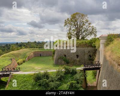 Weit über den Graben zum Tor der Petrovaradin-Festung. Mittelbewölkt, Sonnenreflexionen auf Gras und Wänden. Stockfoto