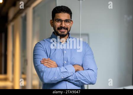 Geschäftsmann mit überkreuzten Armen lächelnd und in die Kamera schauend, Porträt eines glücklichen männlichen Arbeiters im Büro, Chef in Brille und Hemd, glücklich mit den Ergebnissen, stolz und selbstbewusst. Stockfoto