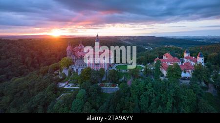 Roter Sonnenuntergang über Schloss Ksiaz, Schloss Fürstenstein, ein wunderschönes Schloss auf einem Felsen, umgeben von Wald. Luftaufnahme, Panoramaaufnahme. Stockfoto