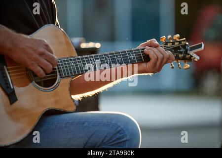 Musiker aus nächster Nähe, der Gitarre beim Gartenfest spielt, sehr farbenfroher, verschwommener Hintergrund, Abend beim Gartenfest. Stockfoto