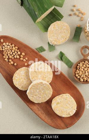 Rohe Tempeh oder Tempe Mentah, Scheiben in ovaler Holzplatte. Tempe ist ein fermentiertes Sojaprodukt, das ursprünglich aus Indonesien stammt. Stockfoto