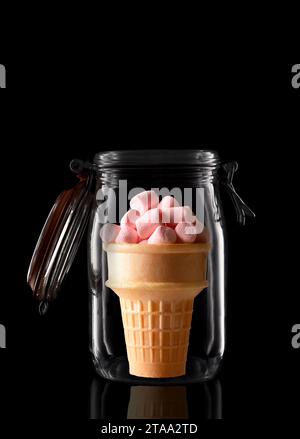 Ein Eiskegel gefüllt mit Marshmallows in einem Vorratsbehälter aus Glas oder einem Dosenbecher, isoliert auf Schwarz mit Reflexion, mit offenem Deckel. Stockfoto