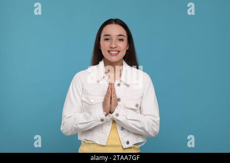 Vielen Dank. Schöne dankbare Frau mit Händen, die auf hellblauem Hintergrund zusammengeschlossen sind Stockfoto