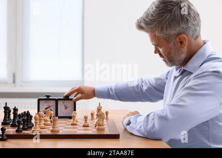 Mann, der während des Turniers am Tisch drinnen die Schachuhr anschaltet Stockfoto