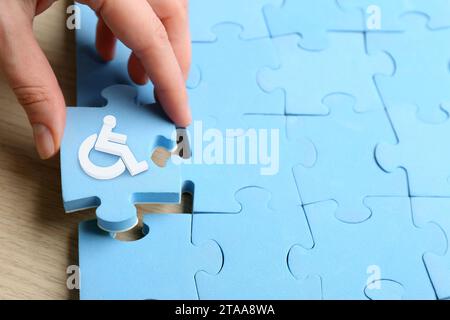 Inklusionskonzept. Frau, die ein hellblaues Puzzle mit internationalem Symbol für den Zugang zusammensetzt, Nahaufnahme Stockfoto