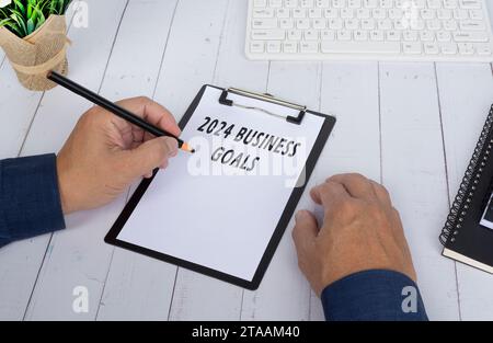 Hände, die 2024 Geschäftsziele auf einer Klemmtafel auf weißem Holzschreibtisch schreiben. Geschäfts- und Finanzkonzept. Stockfoto