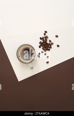Auf weißem und braunem Papierhintergrund, eine köstliche Tasse Kaffee dekoriert mit braunen gerösteten Kaffeebohnen. Kreativer Hintergrund für Werbung. Roa Stockfoto