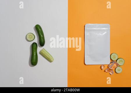 Wenige Gurken auf weißem Hintergrund und ein Maskenpaket mit ices und Gurkenscheiben auf orangefarbenem Hintergrund. Sanftes Pflegekonzept Stockfoto