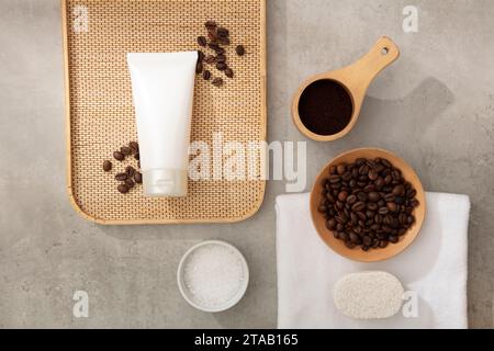 Auf dem Zementboden befindet sich eine weiße Kosmetikröhre, die mit Kaffeebohnen, Kaffeepulver und hölzernen Requisiten dekoriert ist. Modell für Design. Kaffee ist natürlich Stockfoto
