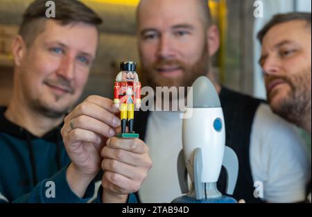 PRODUKTION - 27. November 2023, Sachsen, Seiffen: Holzspielzeughersteller Markus Füchtner (r-l), Tom Neubert und Mario Kaden betrachten den Miniatur-Nussknacker Wilhelm in Markus Füchtners Werkstatt in Seiffen. Der Nussknacker Wilhelm aus dem Erzgebirge ist nach seiner Weltraumreise wieder auf der Erde. Wilhelm wurde 2021 auf die Internationale Raumstation ISS gestartet und verbrachte fast ein Jahr im Weltraum. Astronaut Matthias Maurer nahm die 12 Zentimeter hohe und 29 Gramm schwere Figur mit. Während seiner 350 Tage im Weltraum umkreiste Wilhelm 5573 Mal die Erde. Im August 2022 kehrte er mit dem SpaceX Dragon CRS-25 zurück Stockfoto