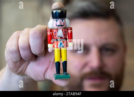 PRODUKTION - 27. November 2023, Sachsen, Seiffen: Holzspielzeughersteller Markus Füchtner hält in seiner Werkstatt in Seiffen den Miniatur-Nussknacker Wilhelm in der Hand. Der Nussknacker Wilhelm aus dem Erzgebirge ist nach seiner Weltraumreise wieder auf der Erde. Wilhelm wurde 2021 auf die Internationale Raumstation ISS gestartet und verbrachte fast ein Jahr im Weltraum. Astronaut Matthias Maurer nahm die 12 Zentimeter hohe und 29 Gramm schwere Figur mit. Während seiner 350 Tage im Weltraum umkreiste Wilhelm 5573 Mal die Erde. Im August 2022 kehrte er mit der SpaceX Dragon CRS-25 zurück. Foto: Hendrik Schmi Stockfoto