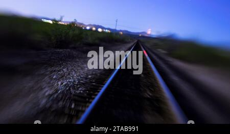 Traumhafte Vision von parallelen Bahngleisen, die die Dunkelheit der Dämmerung absorbieren und in der blauen Stunde der Natur unendlich werden. Stockfoto