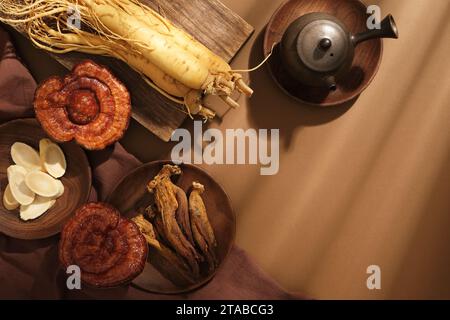 Auf braunem Hintergrund, frische Ginsengwurzeln, Lingzhi-Pilze und roter Ginseng auf Holztablett, dekoriert mit Teekanne. Leerzeichen für die Stockfoto