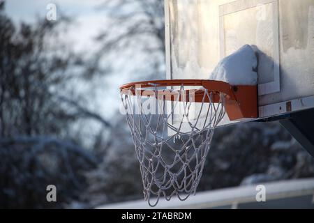Basketballkorb im Freien vor verschwommenem Hintergrund. Das Netz und der Rand des Korbs sind mit einer Schneeschicht bedeckt, die dem Korb eine einzigartige kalte Note verleiht Stockfoto