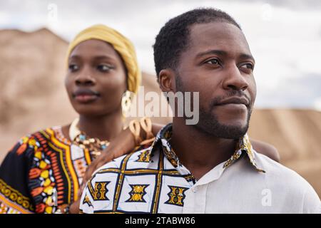 Modeporträt eines afroamerikanischen Paares, das traditionelle Kleidung trägt und in der Wüste posiert, konzentriert sich auf den Mann, der im Vordergrund wegschaut Stockfoto