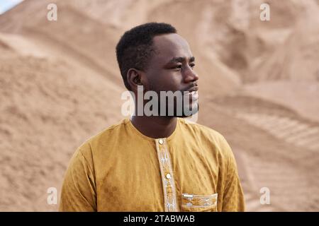 Seitliches Porträt des Schwarzen Mannes, der traditionelle Kleidung trägt und in der Wüste wegschaut, Kopierraum Stockfoto