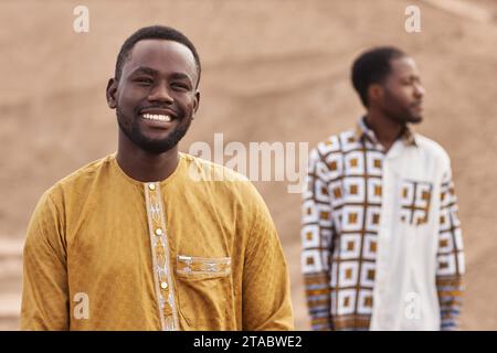 Porträt eines afroamerikanischen Mannes, der traditionelle Kleidung trägt und in der Wüste in die Kamera lächelt, im Kopierraum Stockfoto
