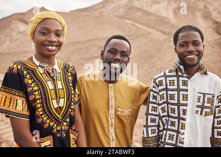 Gruppe junger Afroamerikaner, die traditionelle Kleidung in der Wüste tragen, alle lächeln Stockfoto