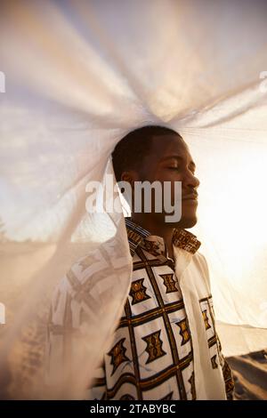 Vertikales Porträt eines afroamerikanischen Mannes, der traditionelle Kleidung trägt und im Freien mit Schleier bedeckt schaut Stockfoto