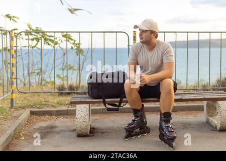 Portrait von Happy stattliche männliche Rolle in Inline Skates sitzt auf der Bank im Park. Stockfoto