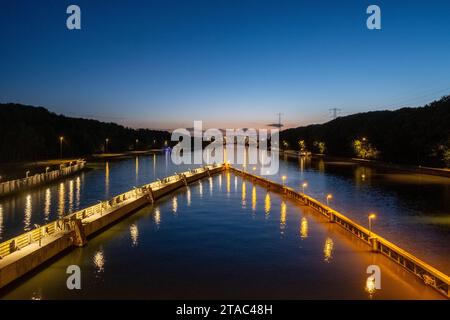 Wenn die Dämmerung absinkt, zeigt dieses Bild einen Flussweg, der von Straßenlichtern beleuchtet wird und einen Lichtweg über das Wasser schafft. Der Fußweg trennt den Fluss symmetrisch und führt das Auge zum urbanen Horizont. Der Himmel, eine Mischung aus dem letzten Licht des Tages und dem Beginn der Nacht, reflektiert sich auf der Wasseroberfläche und harmoniert mit den künstlichen Lichtern. Diese Szene fängt das friedliche Zusammenleben von städtischer Entwicklung und natürlichem Fluss zur magischen Stunde ein. Dämmerung über dem River Walk. Hochwertige Fotos Stockfoto